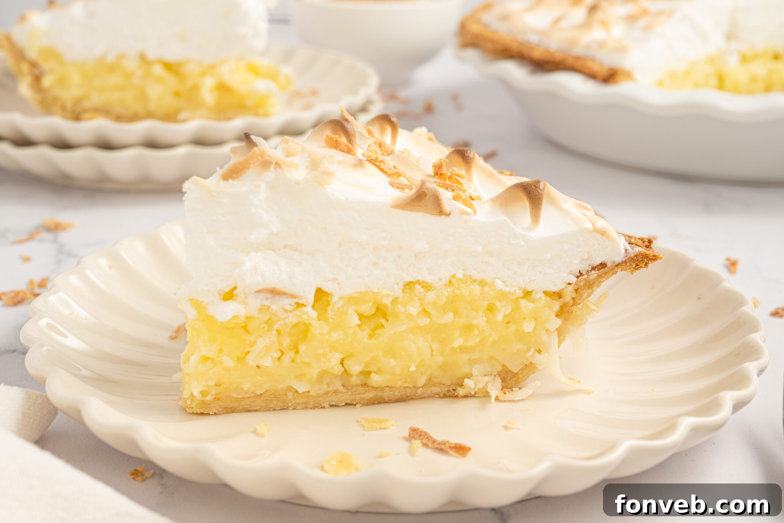 Up close shot of my Coconut Meringue Pie on plate with toasted coconut sprinkled around it on table