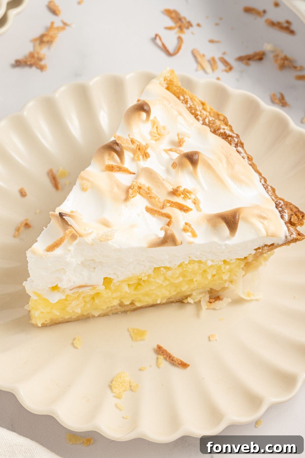 Coconut Meringue Pie on plate with toasted coconut sprinkled around it on table
