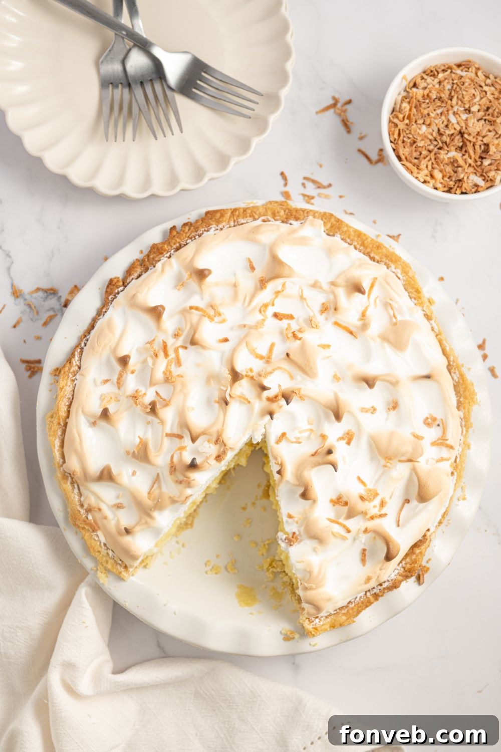 overhead of Coconut Meringue Pie on table with a small plate to the side and toasted coconut flakes