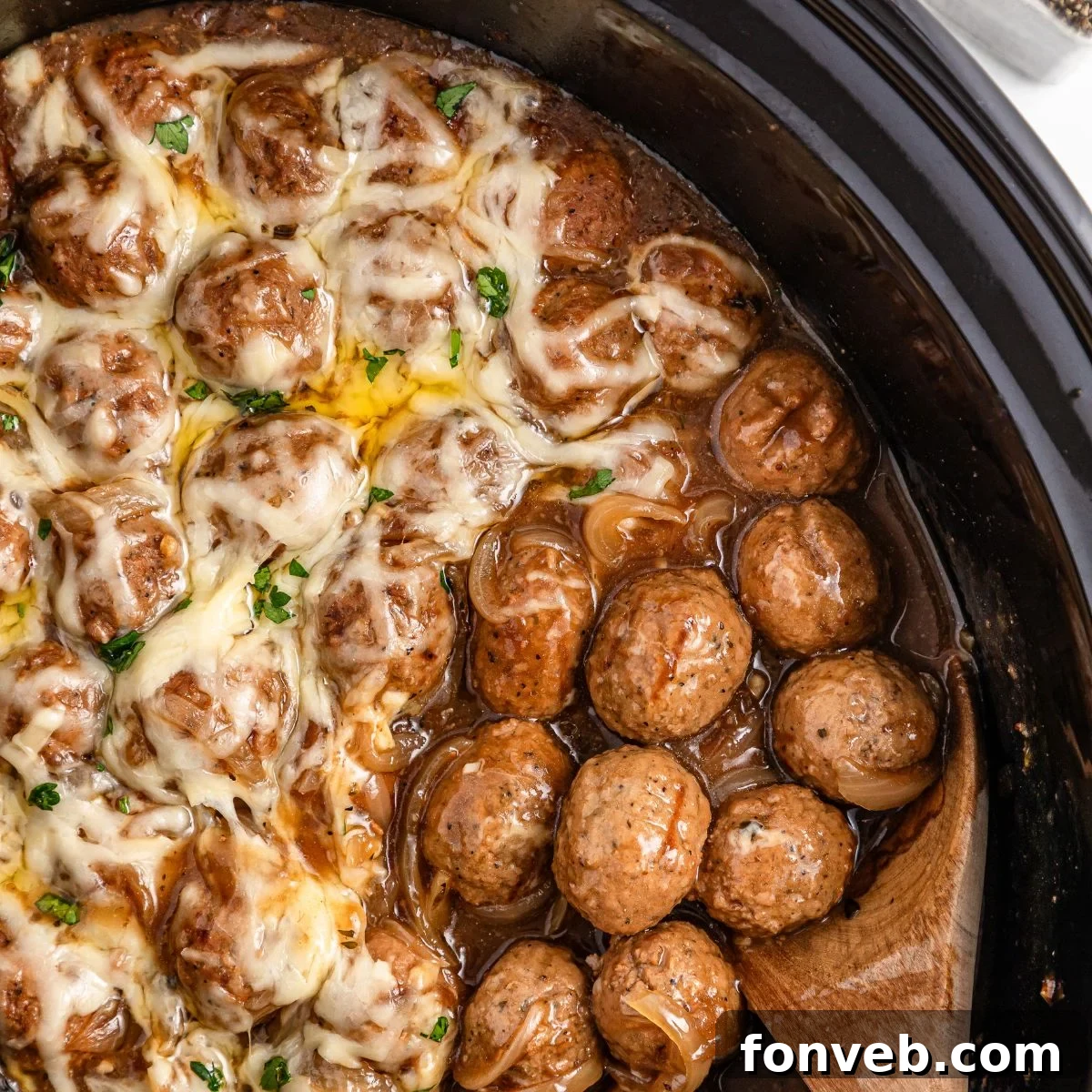 Crock Pot French Onion Meatballs in a slow cooker, with a wooden spoon scooping some up
