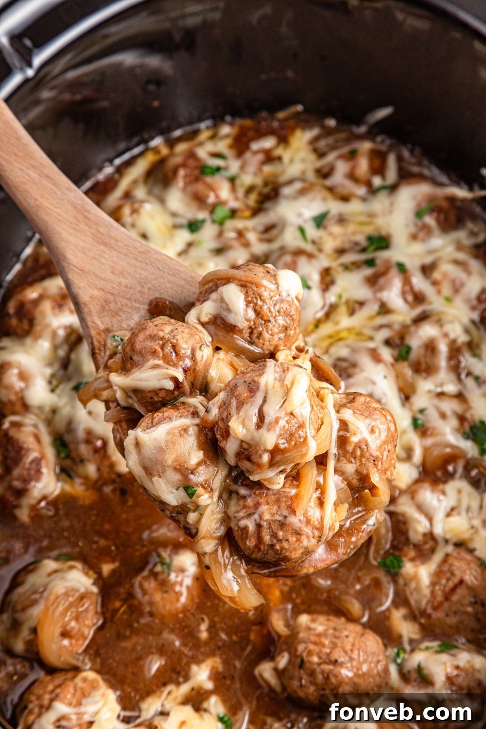 Crock Pot French Onion Meatballs in a slow cooker getting some scooped out with a wooden spoon