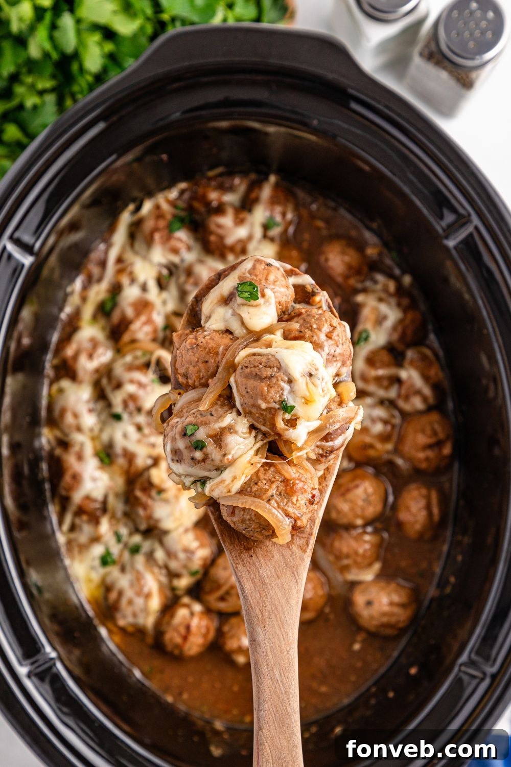 Crock Pot French Onion Meatballs with some being scooped out of slow cooker with spoon 