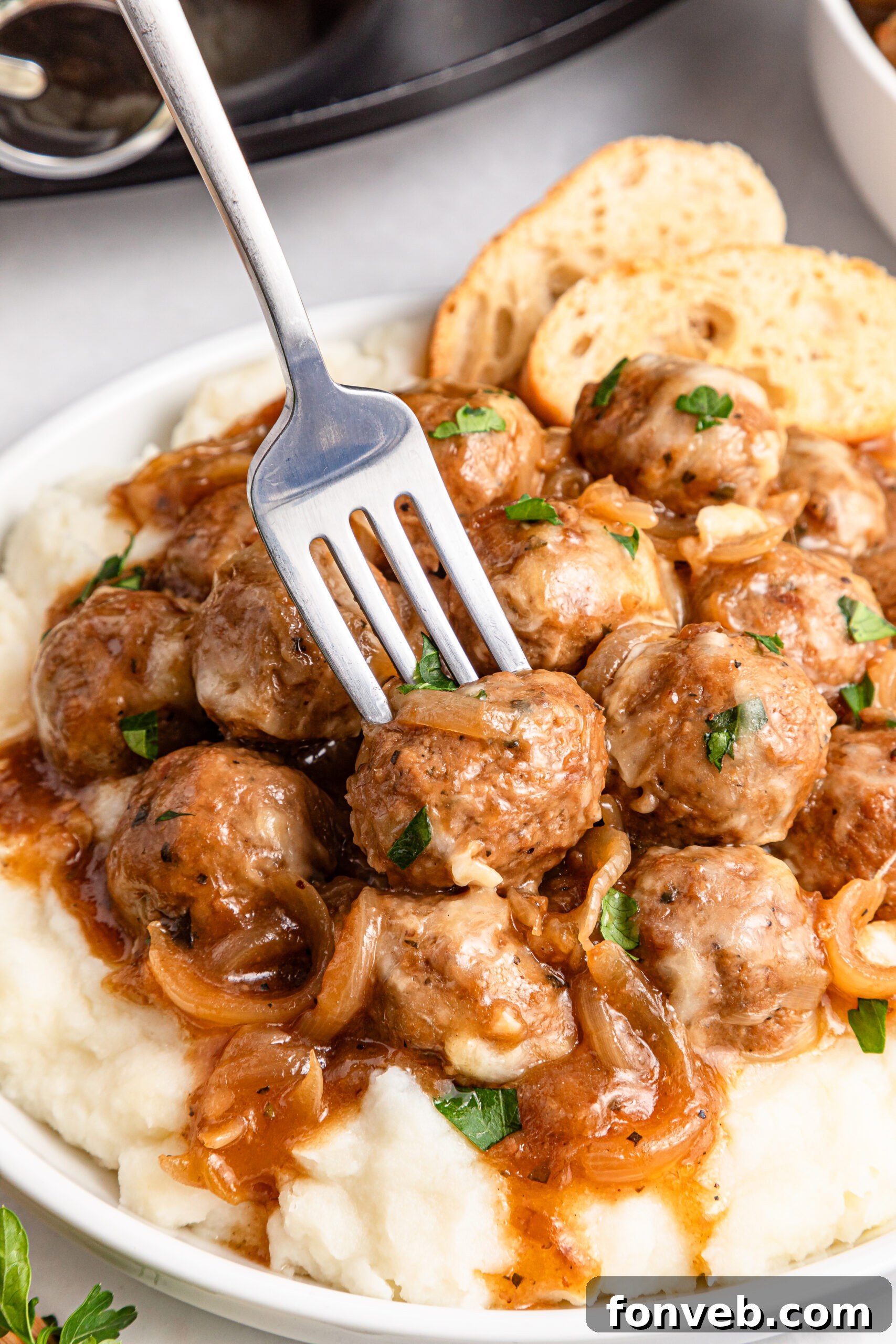 Crock Pot French Onion Meatballs in a white plate with a fork lifting one up