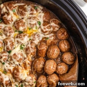 Crock Pot French Onion Meatballs in a slow cooker, with a wooden spoon scooping some up