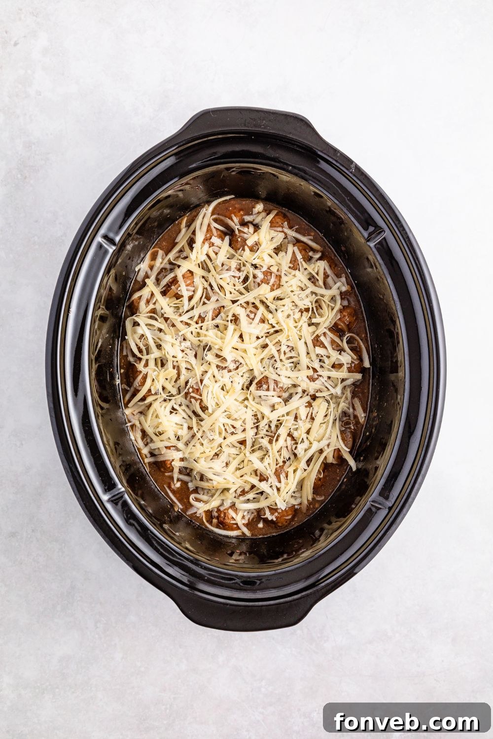 cheese topped French onion meatball mixture in a crock pot 
