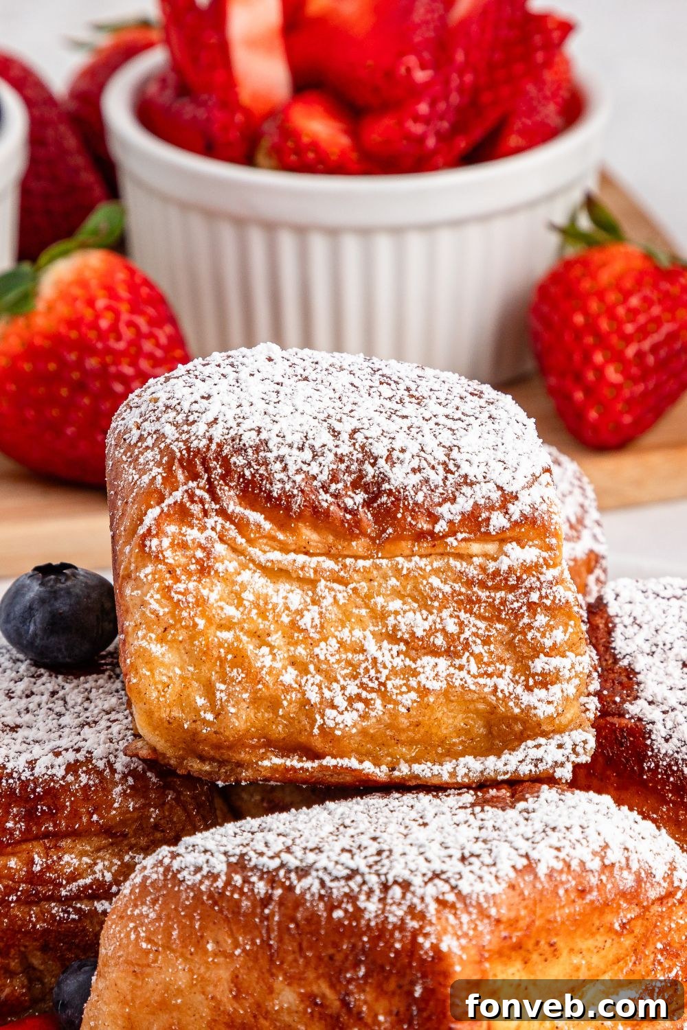 close up of Hawaiian Roll French Toast on a plate with sliced strawberries in a bowl behind it 