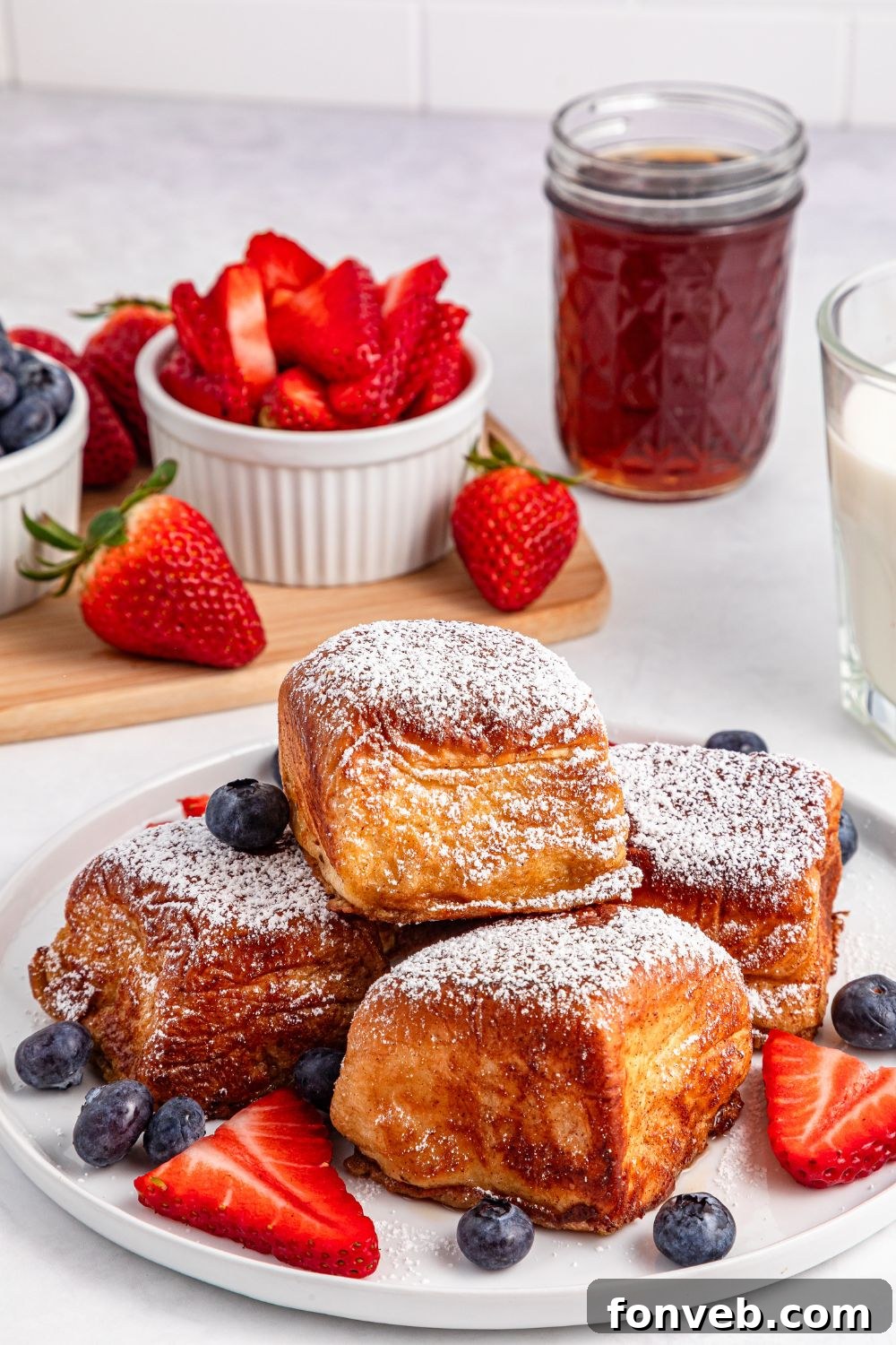 Hawaiian Roll French Toast stacked on plate with berries, and a bowl of strawberries behind it 