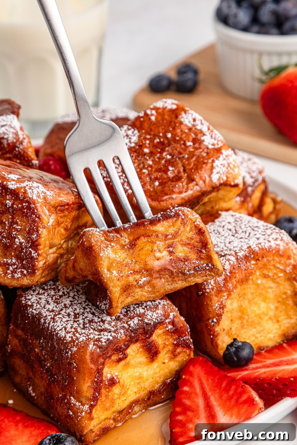 fork poking into a bite of Hawaiian Roll French Toast on plate with strawberries and blueberries 