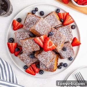 Hawaiian Roll French Toast stacked on a plate with powdered sugar and fruit on top of the French toast