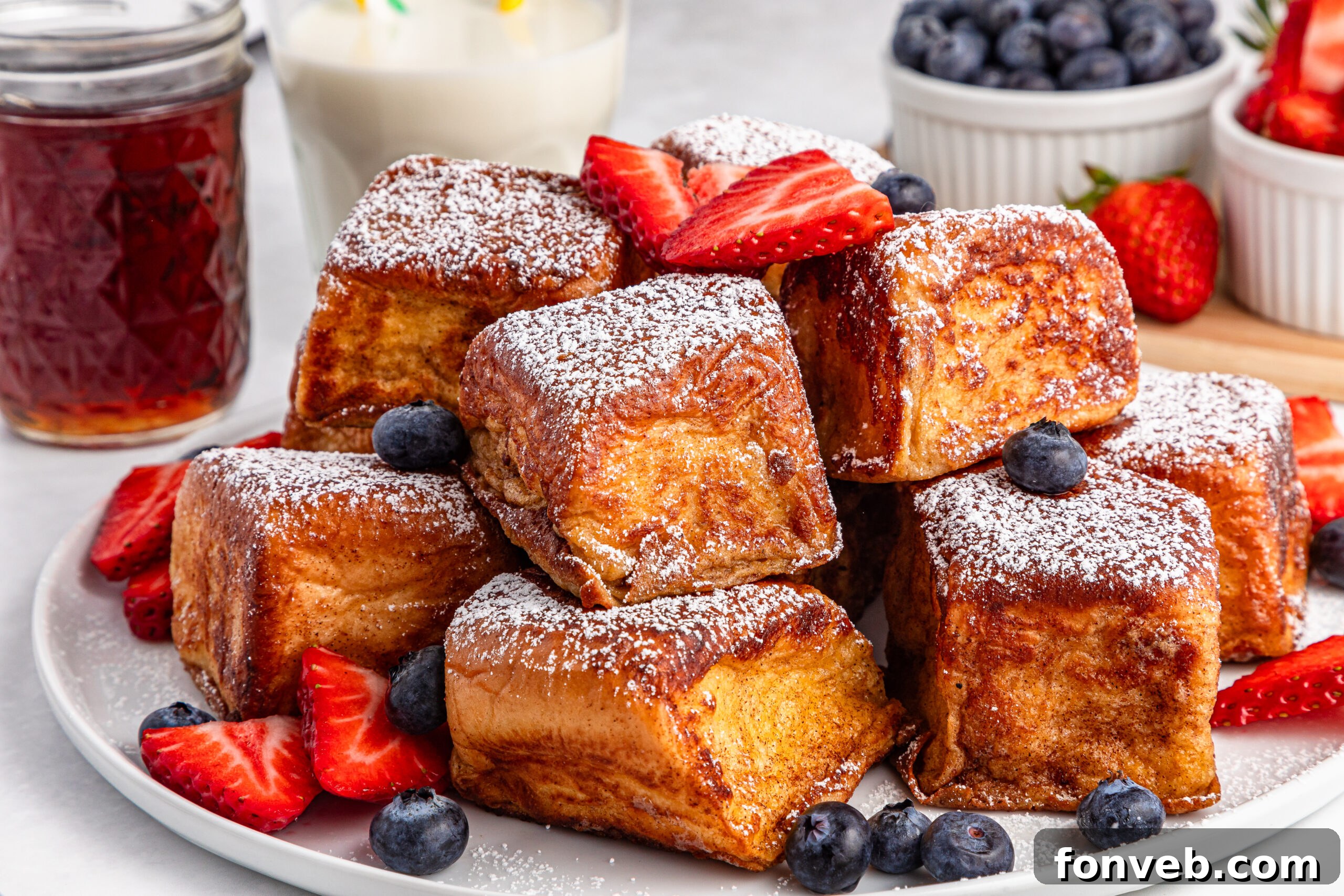 white plate full of the Hawaiian Roll French Toast topped with sliced strawberries and blueberries 