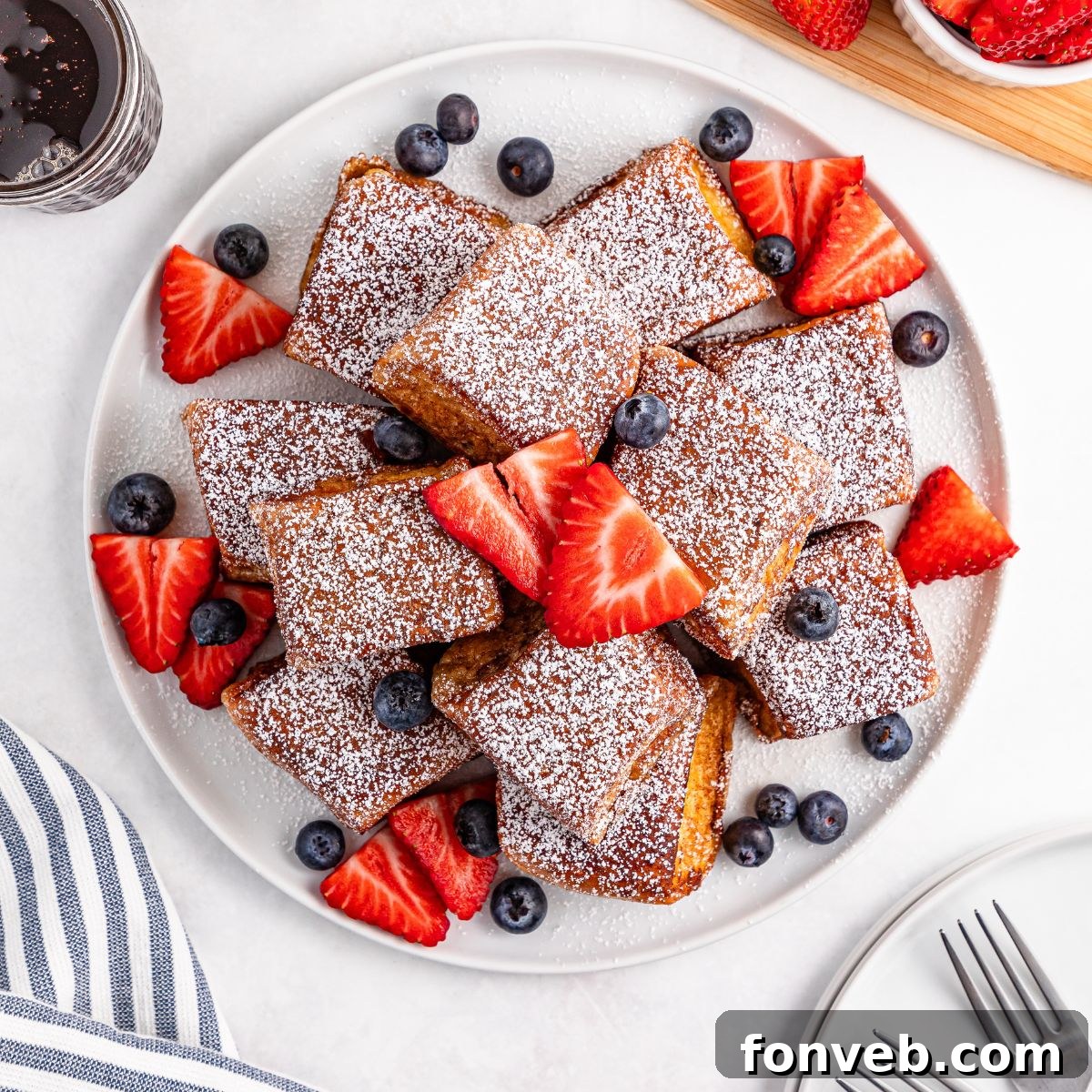 Hawaiian Roll French Toast stacked on a plate with powdered sugar and fruit on top of the French toast