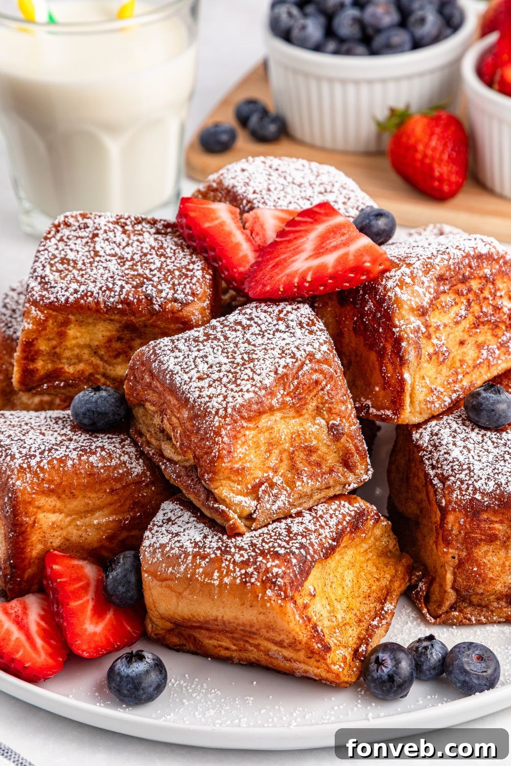 Hawaiian Roll French Toasts stacked on a plate with fruit around it 