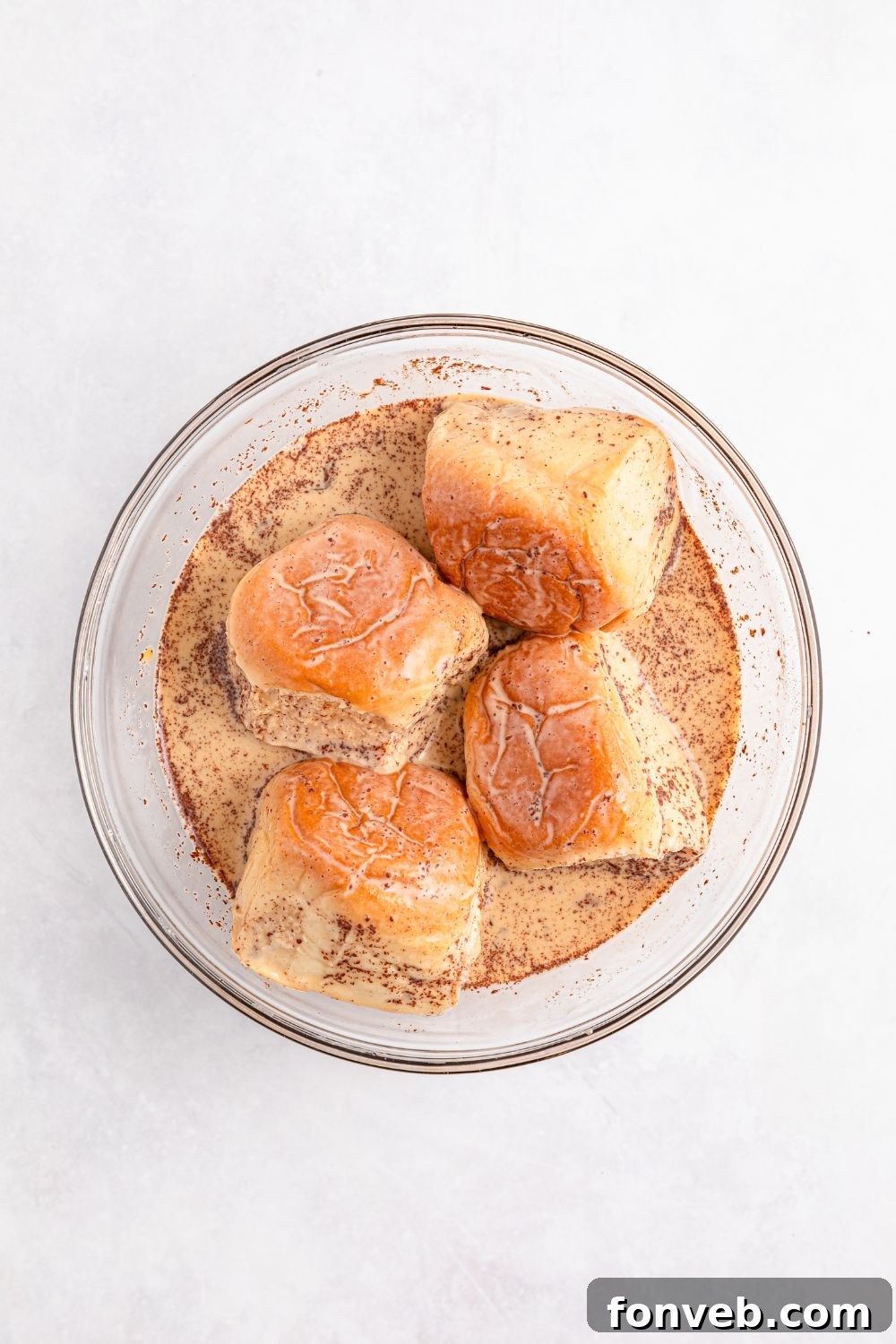 Hawaiian sweet rolls soaking in a French toast mixture in a glass bowl on table 