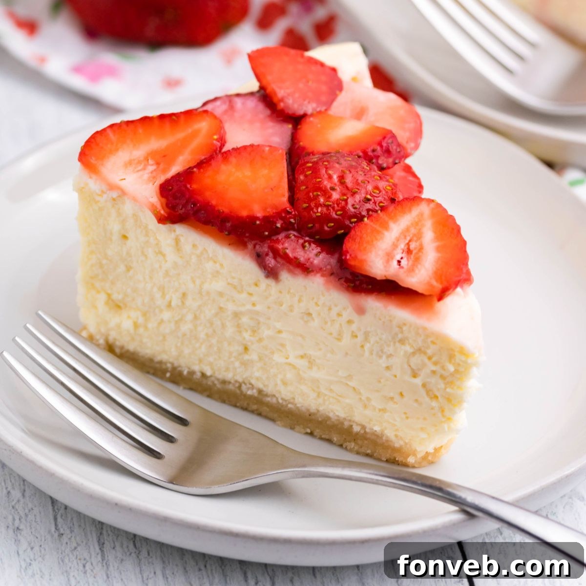 slice of keto cheesecake on a plate topped with strawberries and fork on the side of plate 