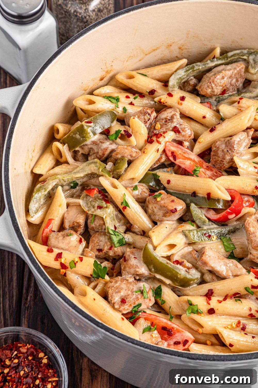 Reggae Ragu 21 Rasta Pasta in a pot on table with a small bowl of red pepper flakes to the side of pot