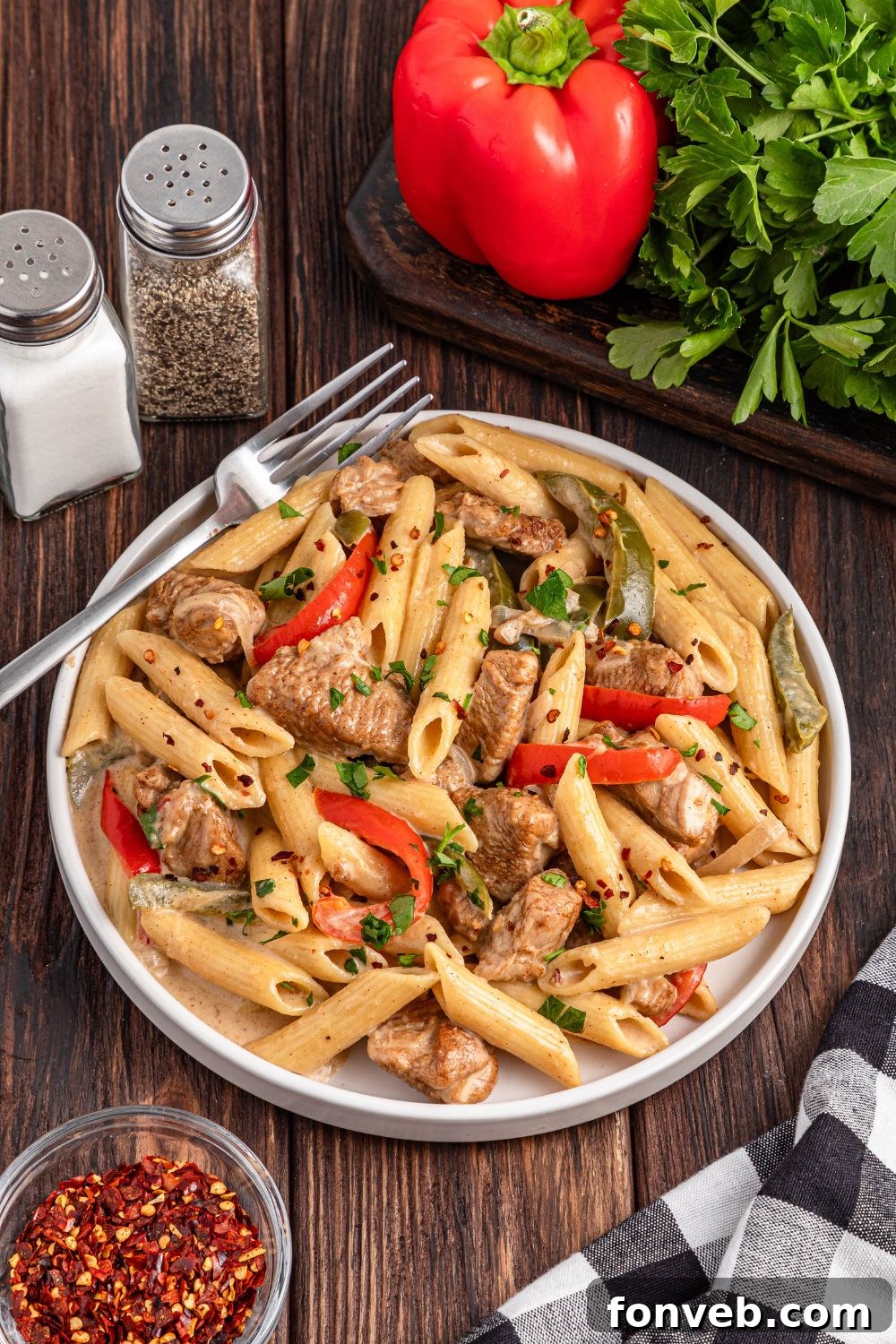 Reggae Ragu 8 Rasta Pasta on a plate with a fork on side, fresh produce, and salt and pepper shaker on table by the plate