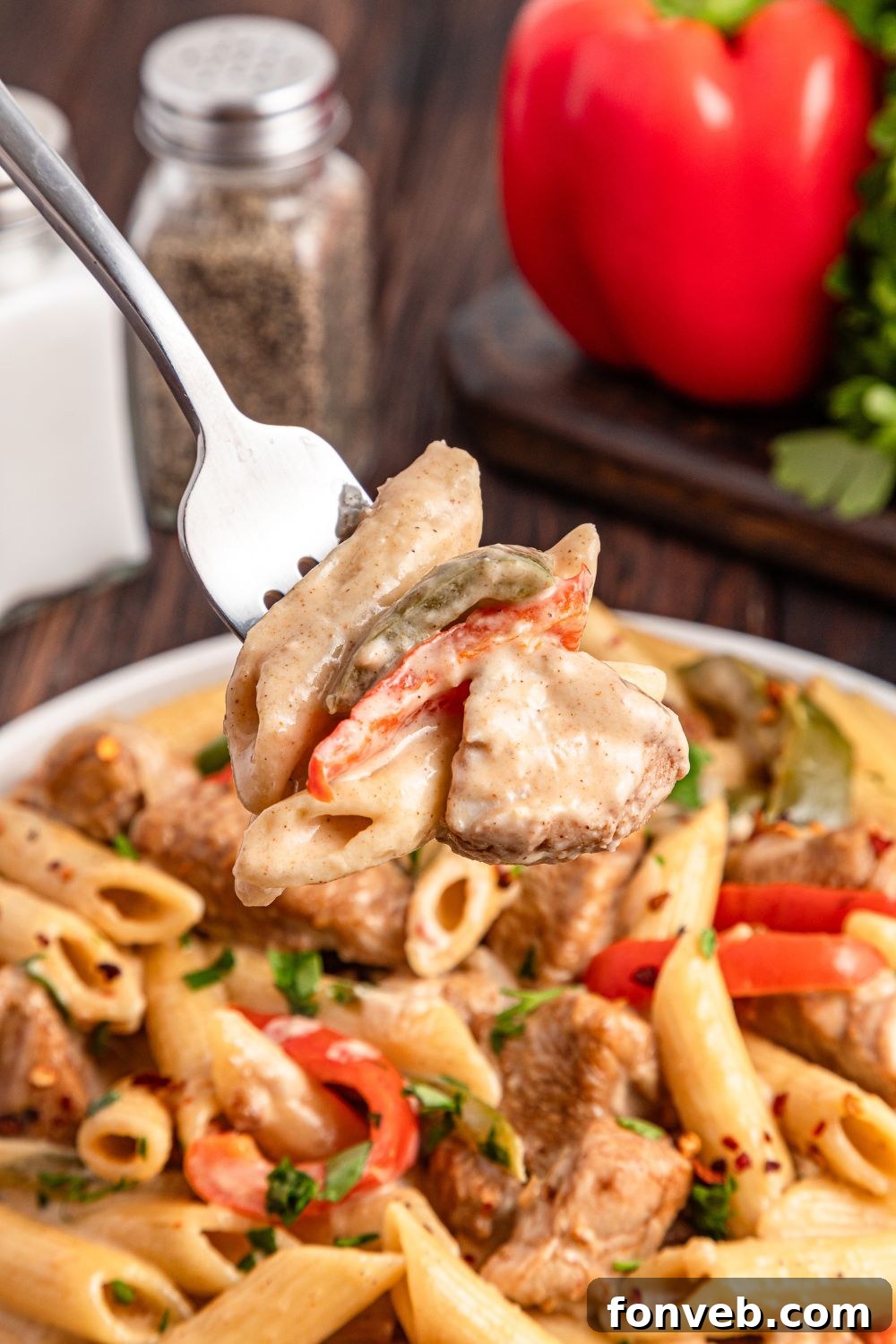 Reggae Ragu 9 fork with a bite of rasta pasta on it, sitting above a bowl of pasta on table