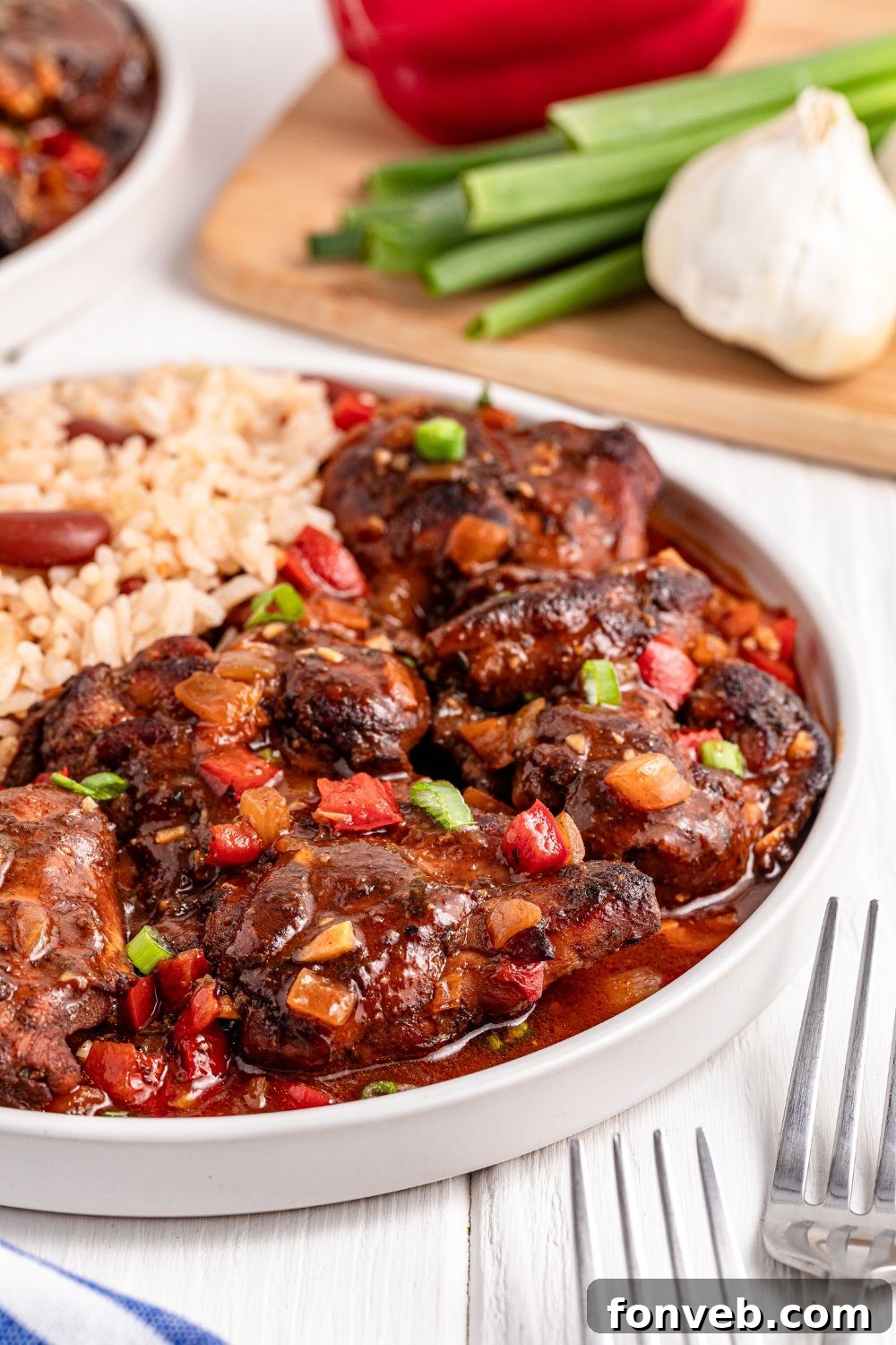 Jamaican Brown Stew Chicken on plate with rice on side and fresh veggies to the side of plate 