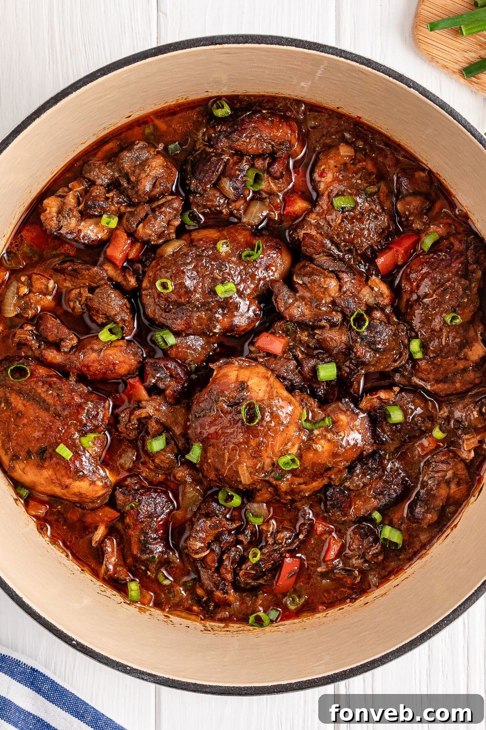 Jamaican Brown Stew Chicken in pot sitting on table with a towel to side 