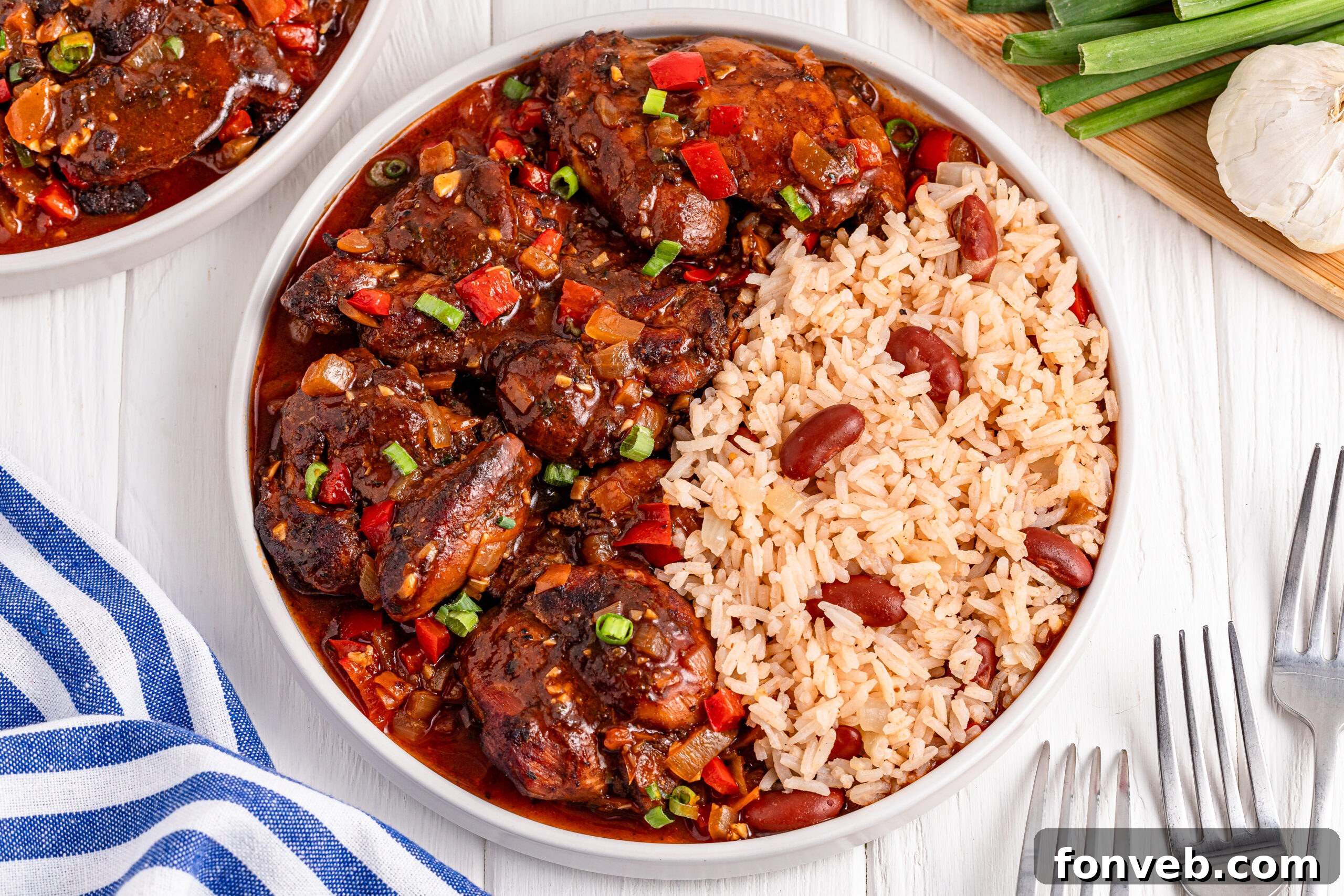 Jamaican Brown Stew Chicken in a white bowl with a side of rice and beans