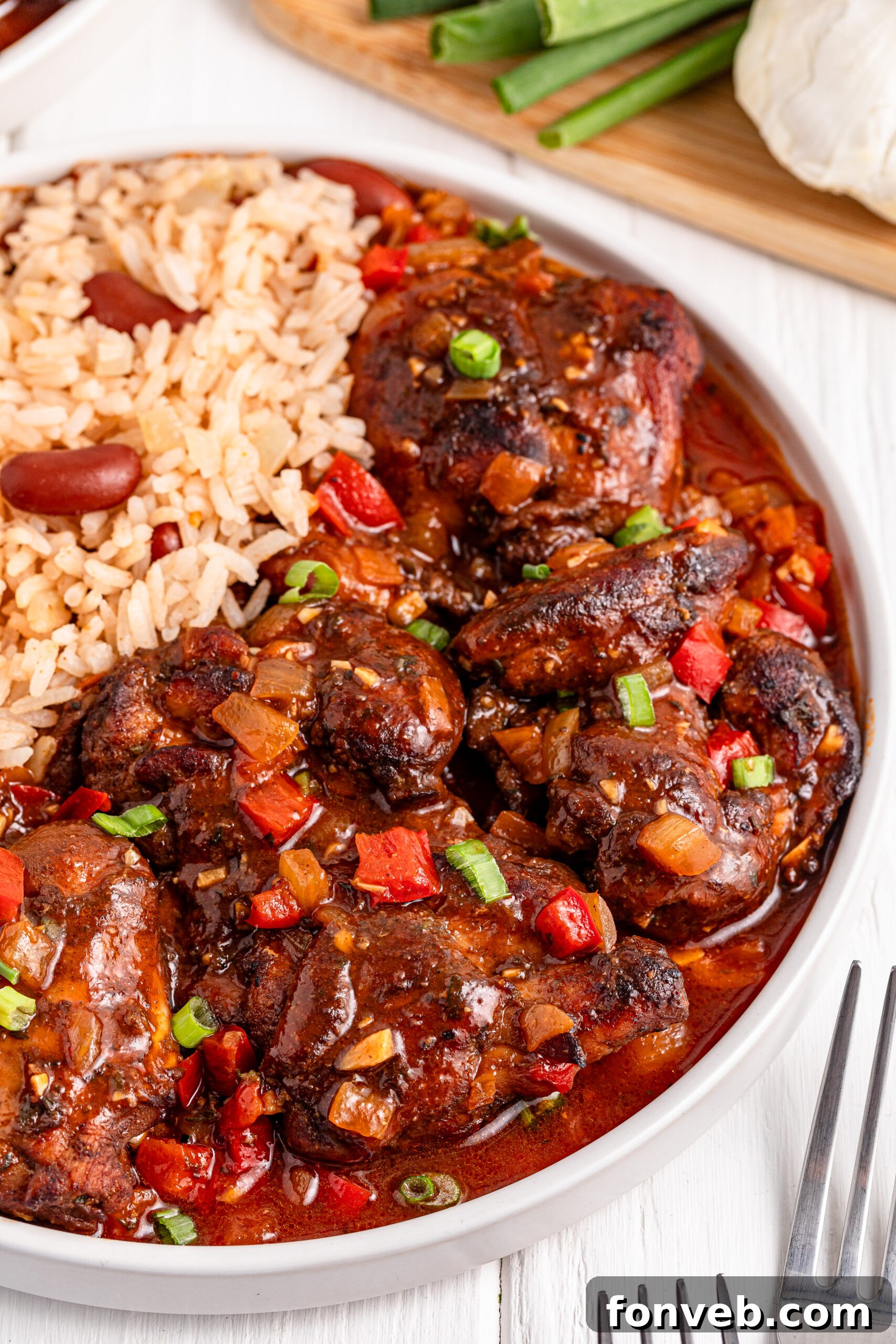 up close view of Jamaican Brown Stew Chicken in a white bowl with a side of rice and beans