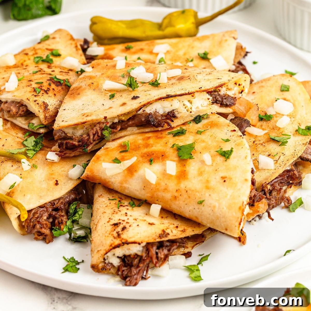 Hearty Mississippi Melt Quesadillas 2 Mississippi Pot Roast Quesadillas stacked on a plate with cilantro and onions on top