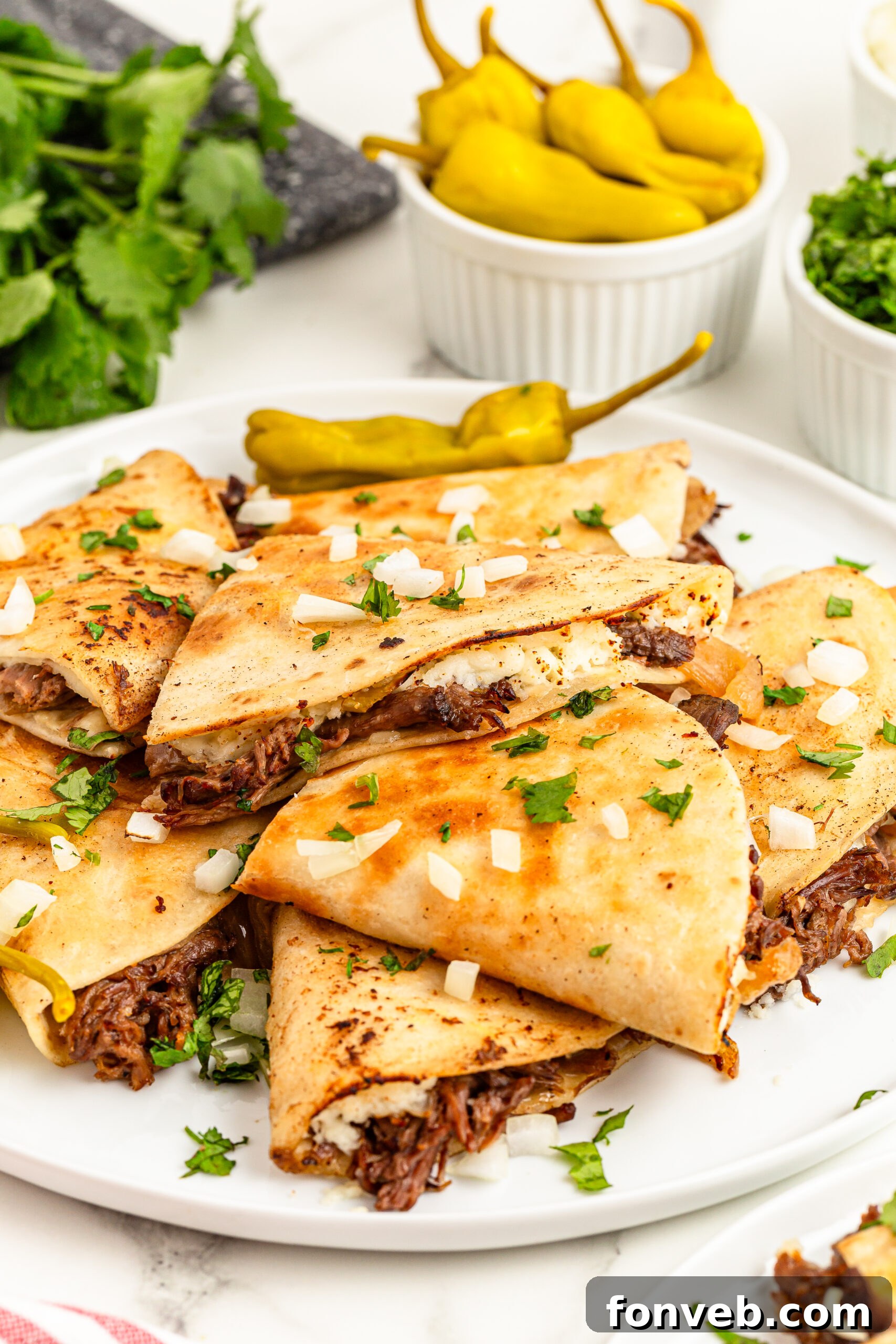 Hearty Mississippi Melt Quesadillas 6 Mississippi Pot Roast Quesadillas piled on a plate with a bowl of peppers in the background