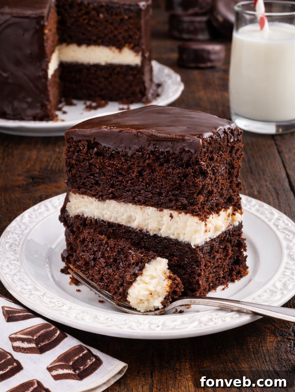 Decadent Chocolate Cream Dream 2 A perfectly sliced Ding Dong Cake on a pristine white plate, with the majestic whole cake elegantly blurred in the background, showcasing its decadent layers and glossy chocolate glaze.
