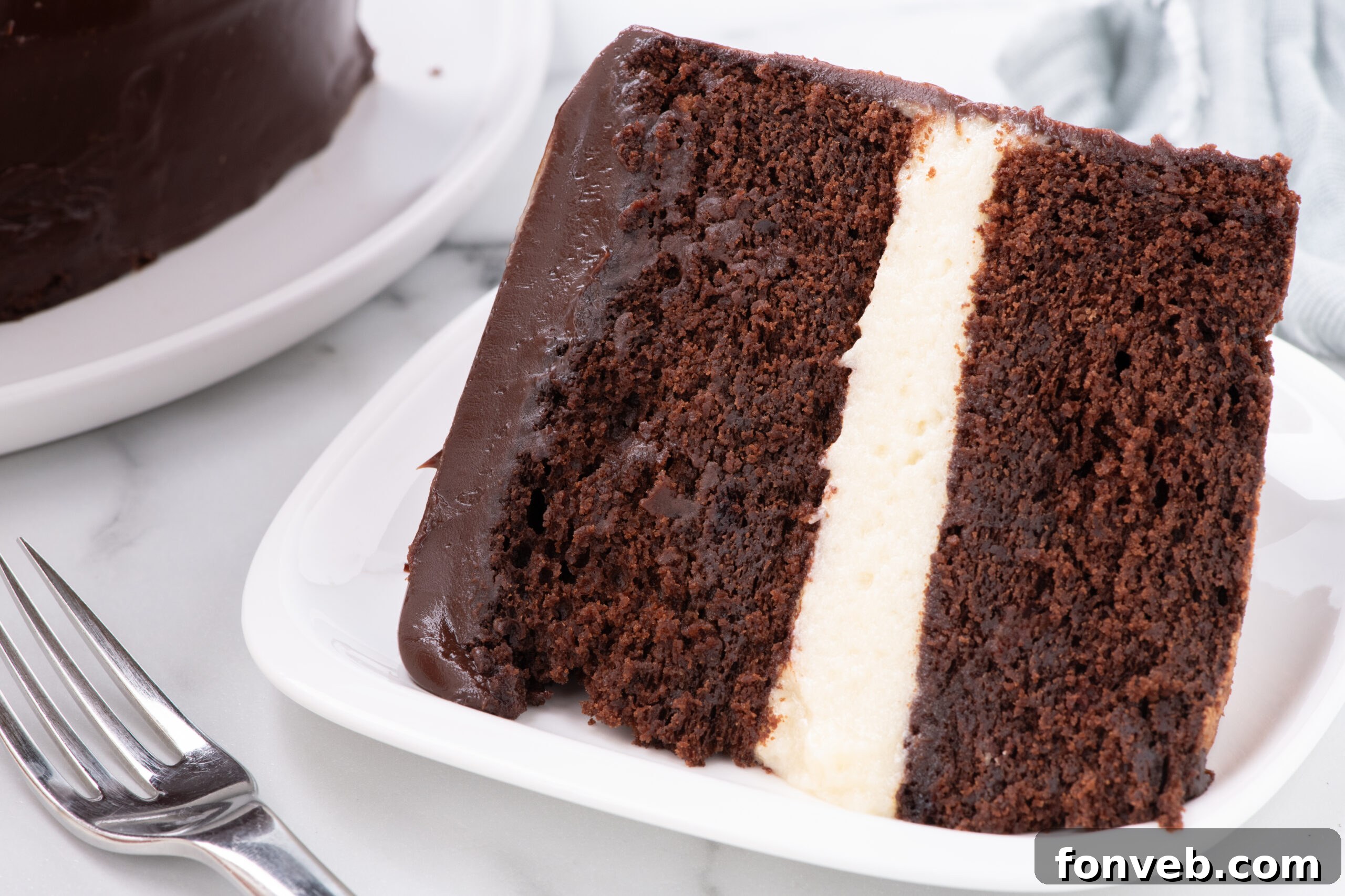 Decadent Chocolate Cream Dream 4 A delectable side view of a slice of Ding Dong Cake presented on a white plate, accompanied by a fork, emphasizing the distinct layers of chocolate cake, creamy filling, and shiny ganache.