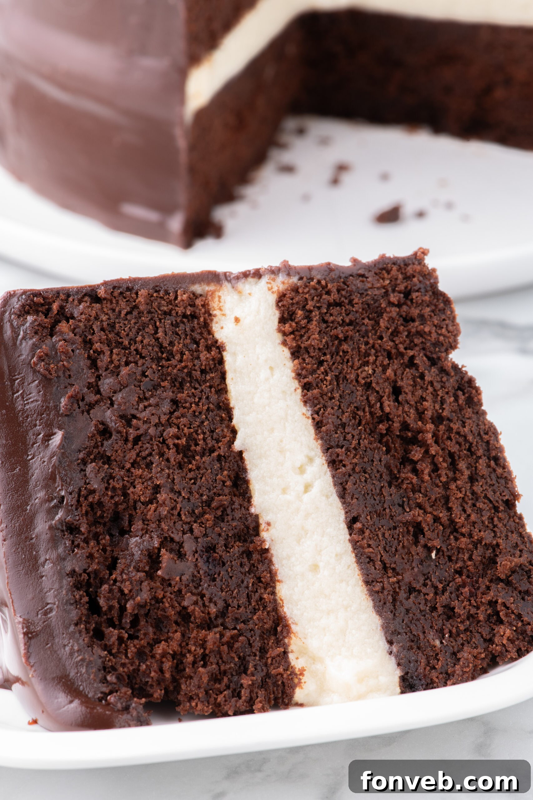 Decadent Chocolate Cream Dream 8 A very close-up and inviting angle of a slice of Ding Dong Cake on a white plate, with the entire cake subtly visible in the background, drawing attention to the intricate layers and smooth texture.