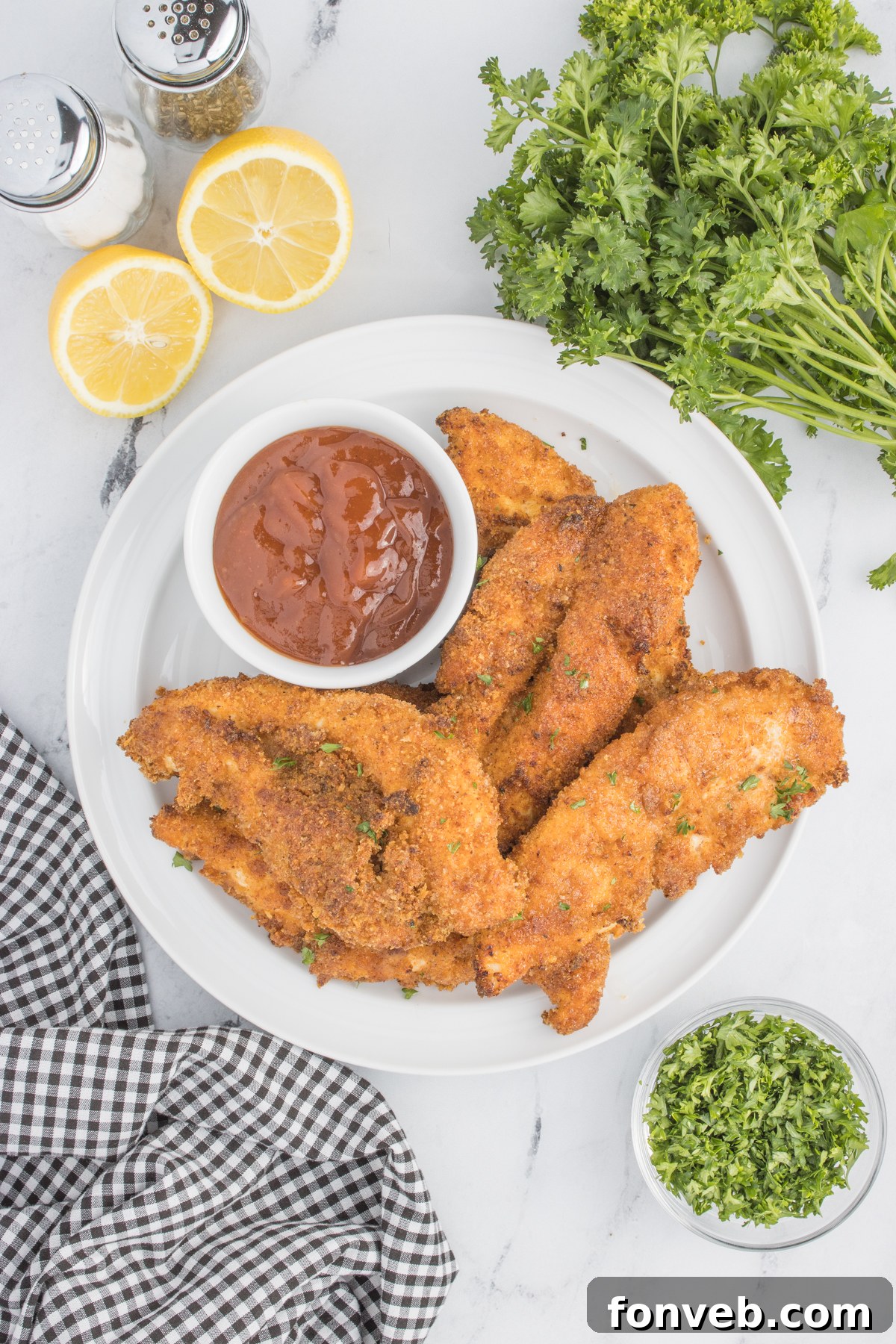 Ultra Crispy Air Fryer Chicken Tenders 3 Overhead view of a pristine white plate laden with golden Air Fryer Chicken Tenders, accompanied by a small container of rich BBQ sauce