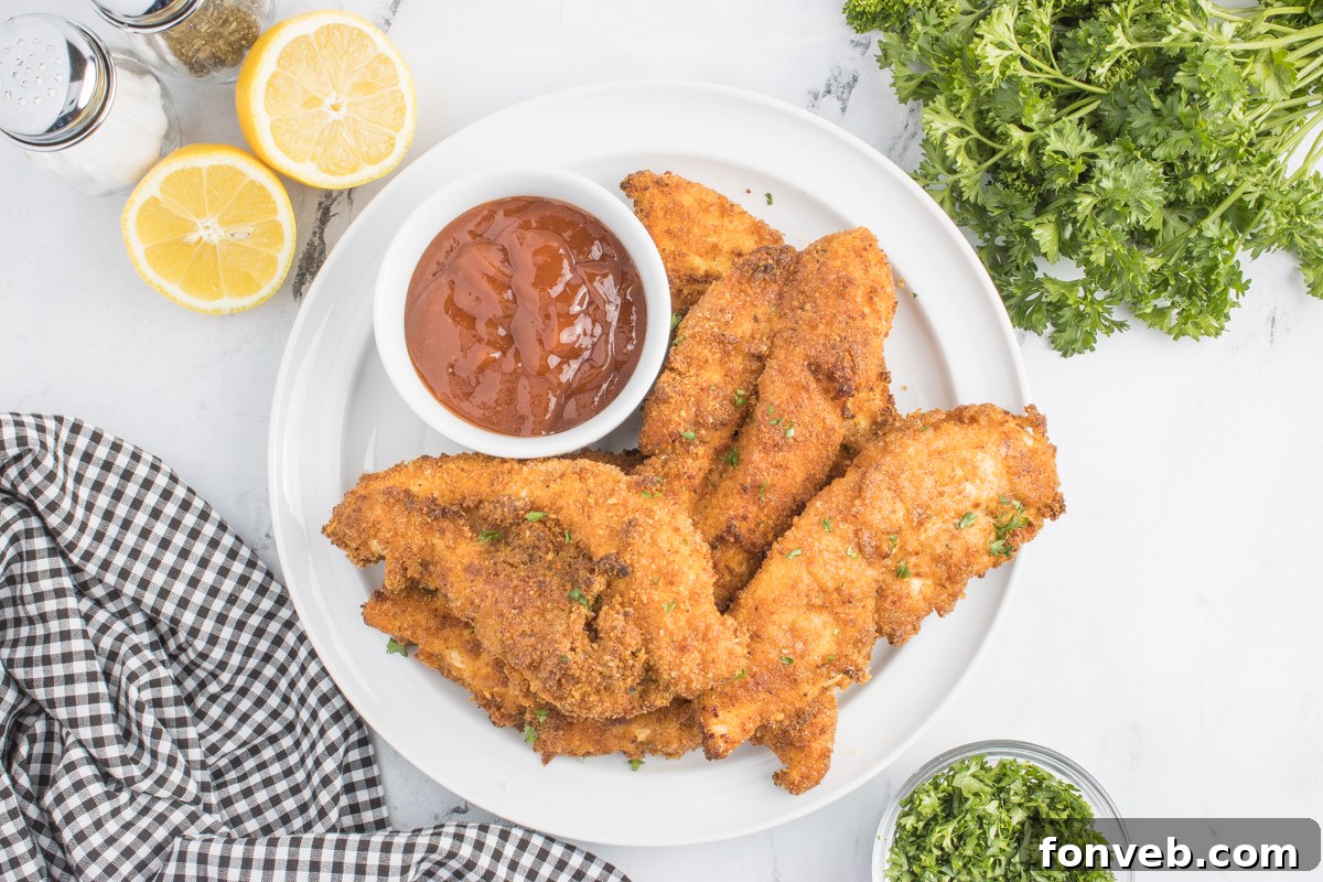 Ultra Crispy Air Fryer Chicken Tenders 10 Overhead shot of perfectly crispy Air Fryer Chicken Tenders on a white plate with a side of BBQ sauce