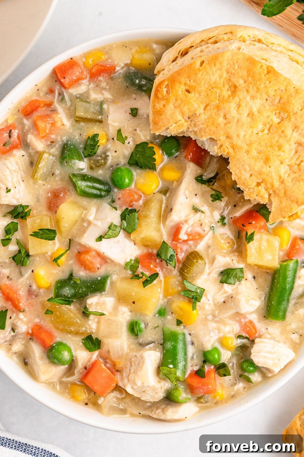 Easy Slow Cooker Chicken Pot Pie 14 Slow Cooker Chicken Pot Pie in a bowl with some bites taken out of a biscuit on side of bowl