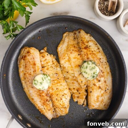 Pan Fried Tilapia in a skillet with lemon butter on top and lemon on side