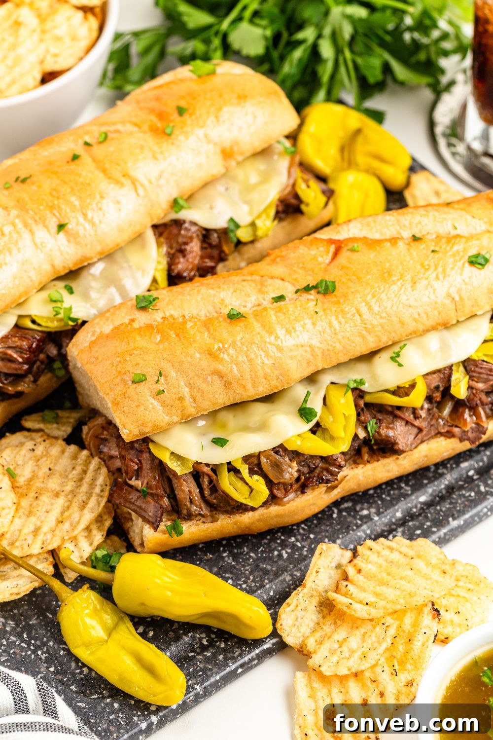 Ultimate Mississippi Pot Roast Sandwiches 18 Mississippi beef sandwiches and peppers on table with some chips and a bowl of au jus on side