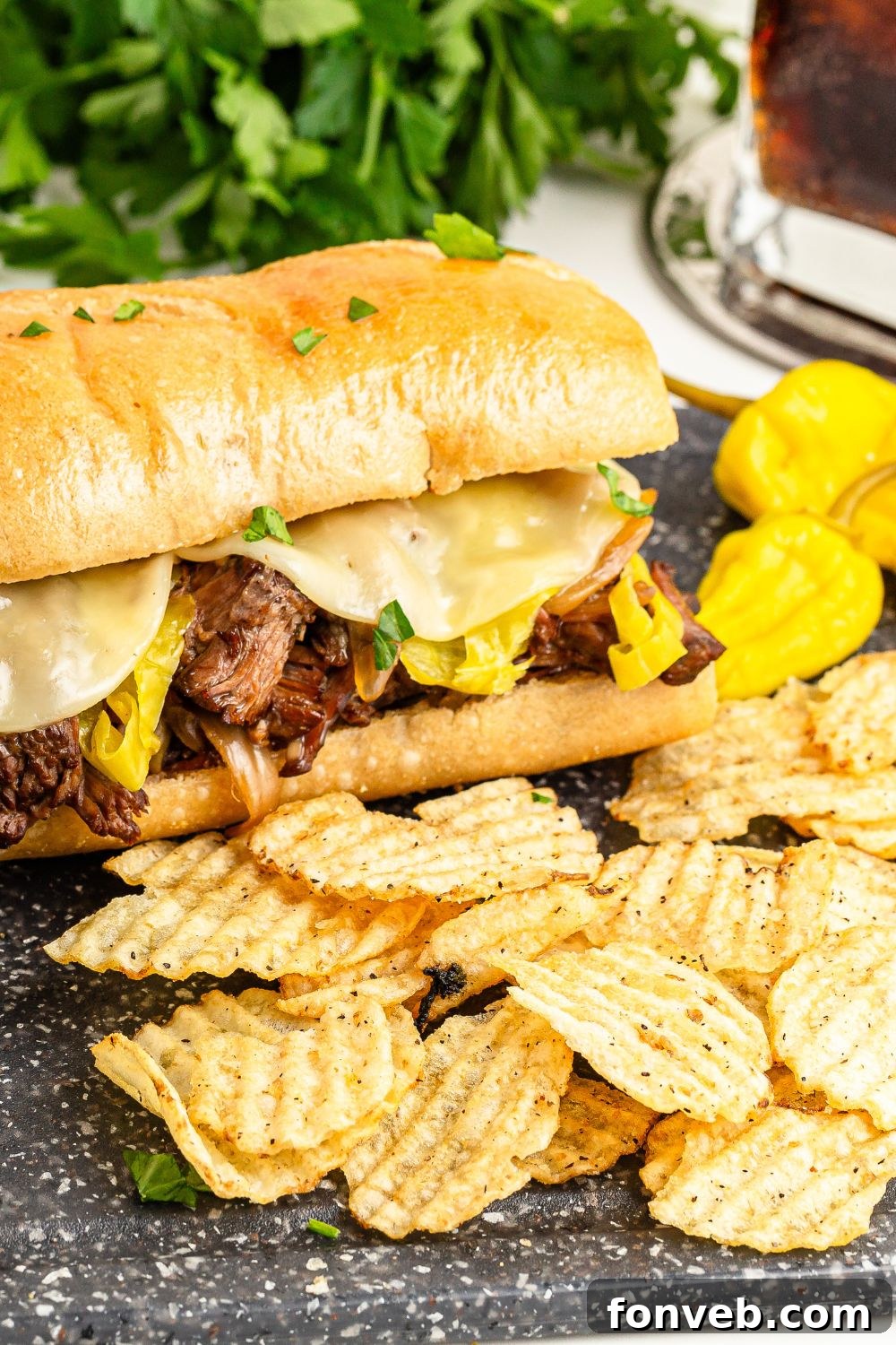 Ultimate Mississippi Pot Roast Sandwiches 19 Mississippi Pot Roast Sandwich on table with some chips and peppers to the side of sandwich