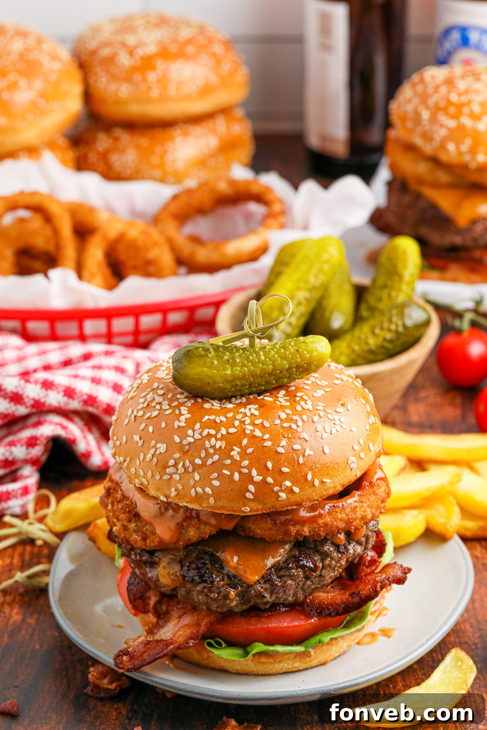 Chuck Wagon Burger 2 A fully loaded Cowboy Burger on a white plate with pickles and fries in the background, showcasing its impressive height and delicious toppings.