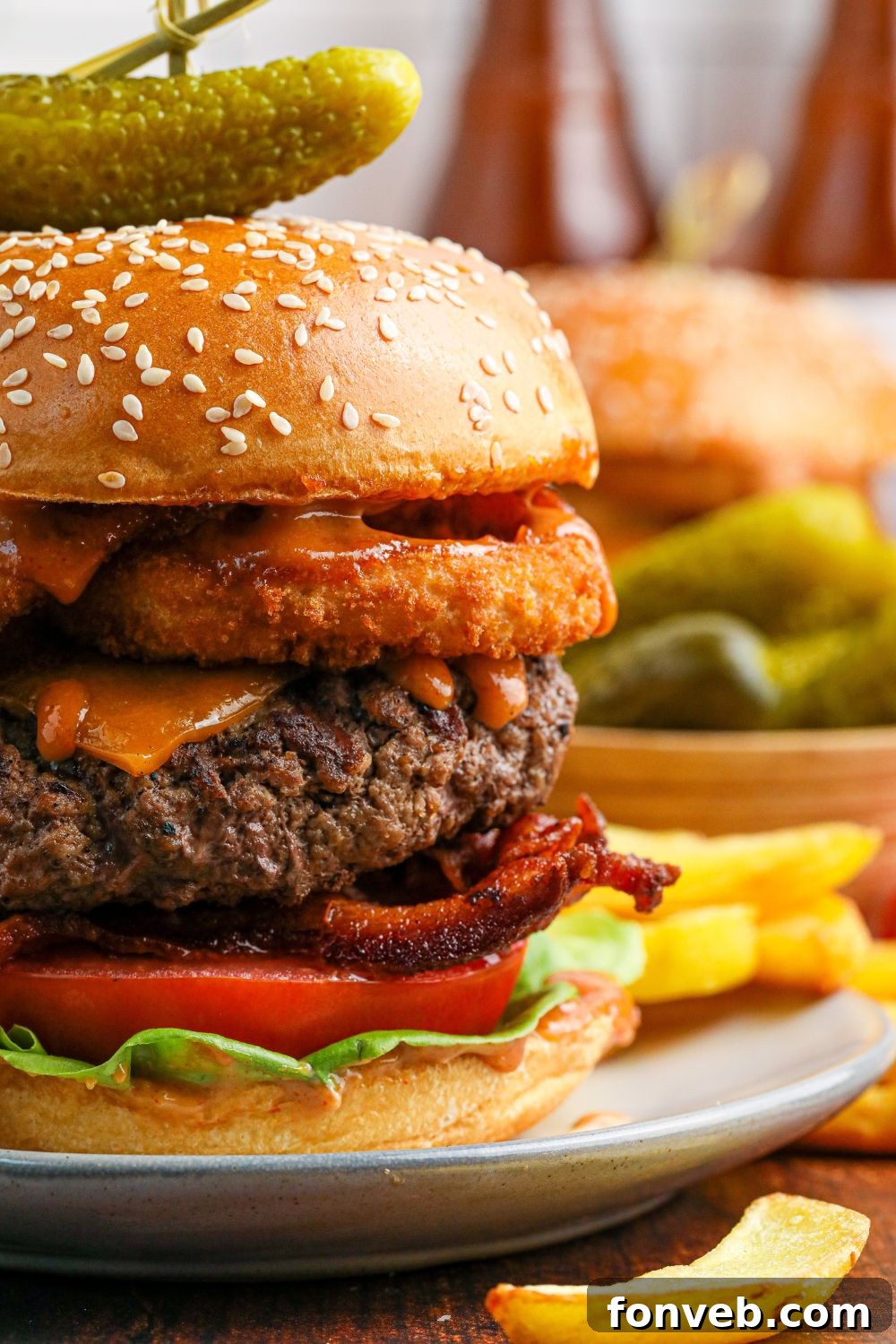 Chuck Wagon Burger 14 A detailed side view of a Cowboy Burger on a plate, showcasing the distinct layers of meat, cheese, bacon, and onion rings.