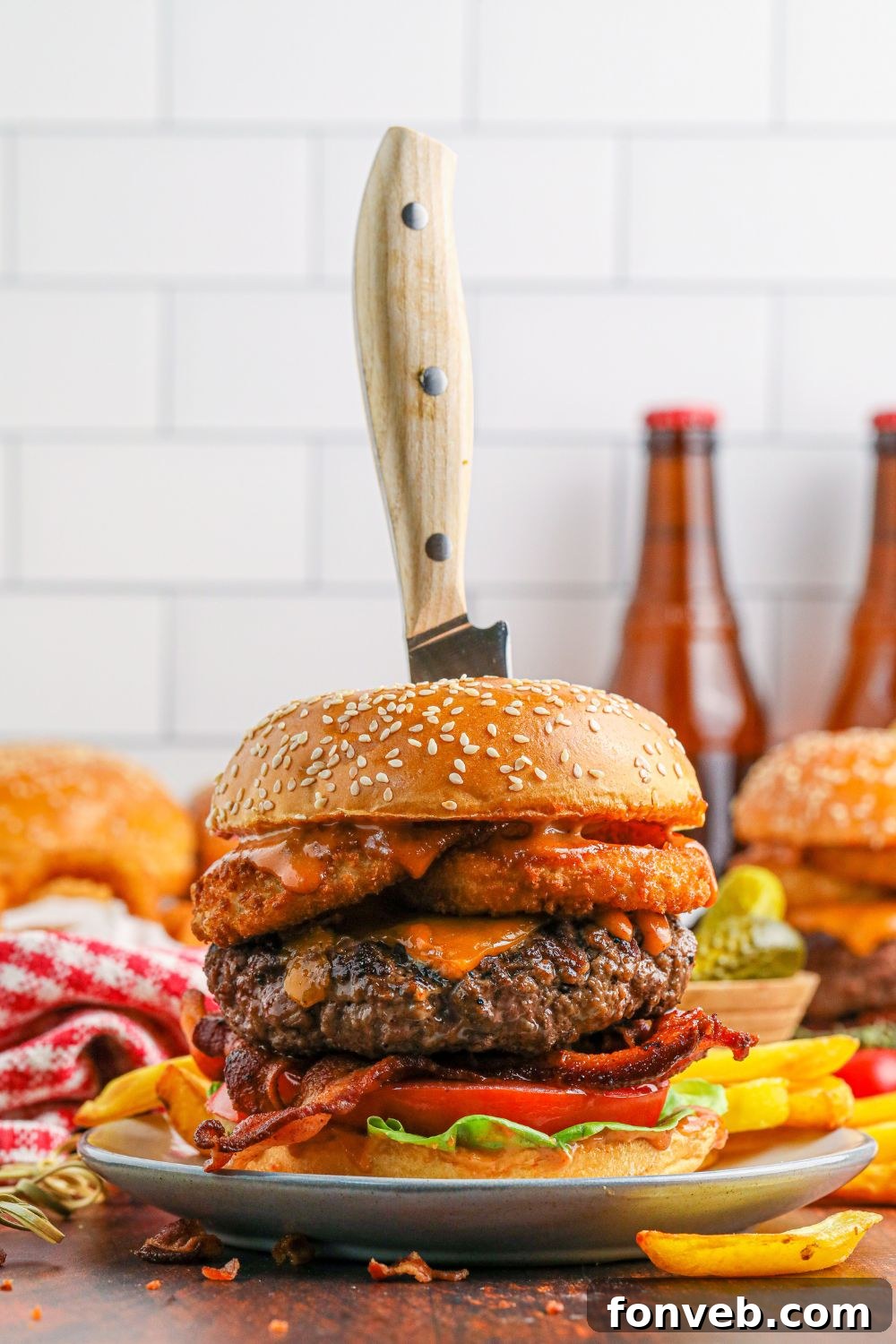 Chuck Wagon Burger 18 Two Cowboy Burgers on plates with knives stabbed into their centers, dramatically showcasing their impressive thickness and height.