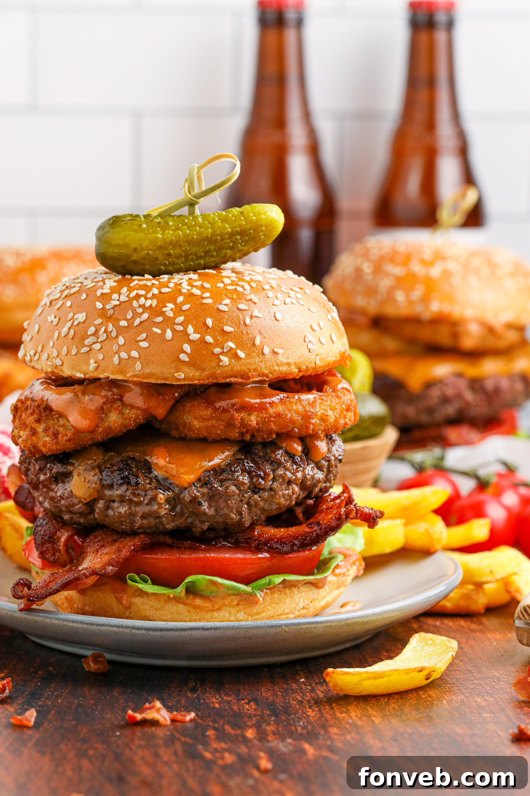 Chuck Wagon Burger 5 A close-up side view of a Cowboy Burger, focusing on the texture of the onion rings, bacon, and melted cheese, with a small pickle on top.