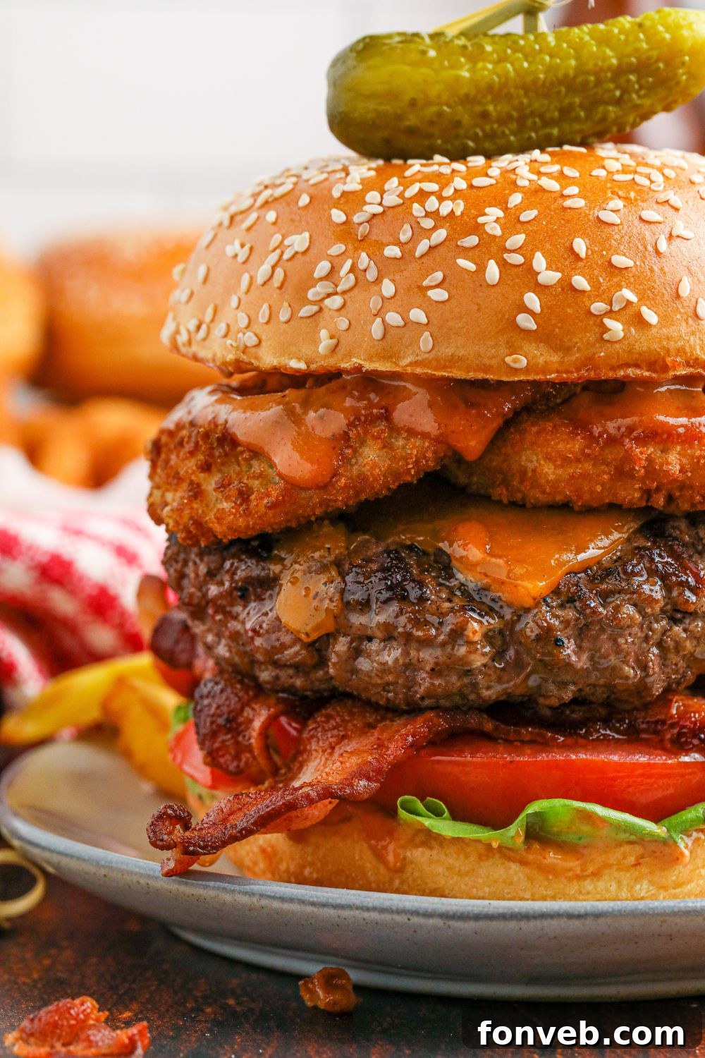 Chuck Wagon Burger 7 An up-close shot of a Cowboy Burger on a plate with a pickle spear on top, emphasizing its intricate layers and inviting texture.