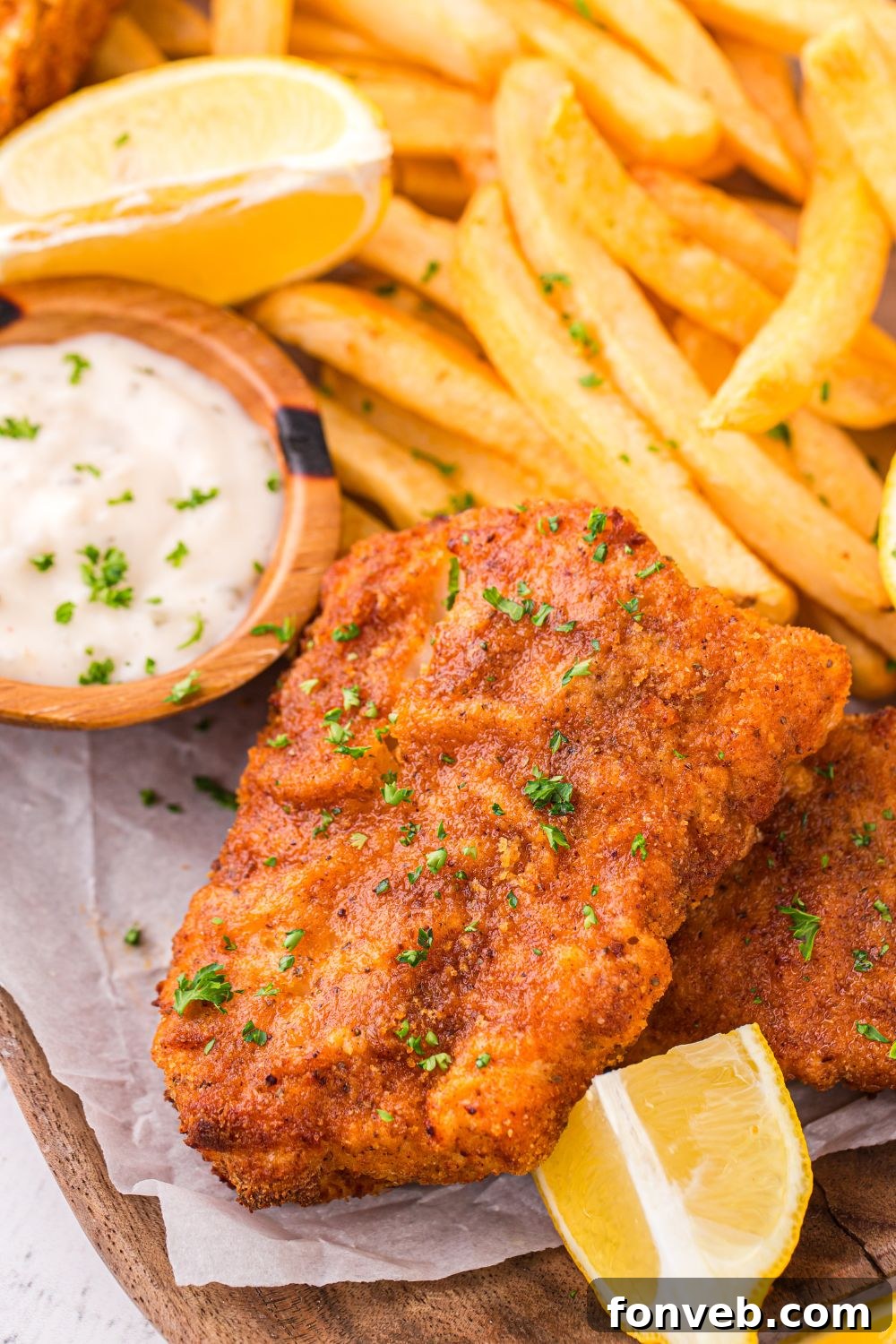 Crispy Air-Fried Fish and Chips 6 Air Fryer Fish And Chips on a table with some parchment paper under it with lemon wedges and tartar sauce