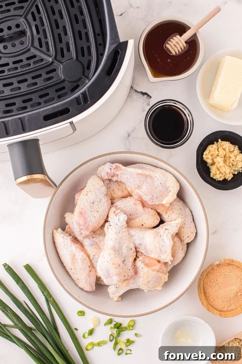 ingredients for Air Fryer Honey Chicken Wings on table in single serve bowls with an air fryer to the side of image 