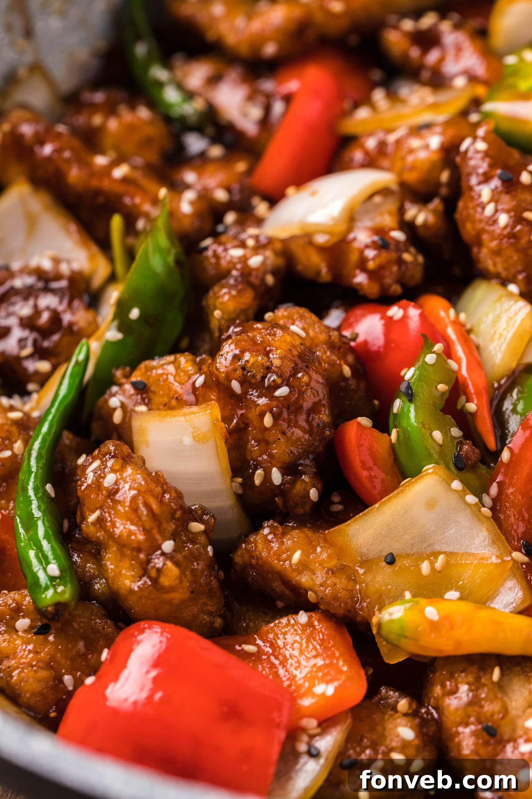 Up close shot of the crispy, saucy General Tso Chicken simmering in a skillet, garnished with fresh scallions.