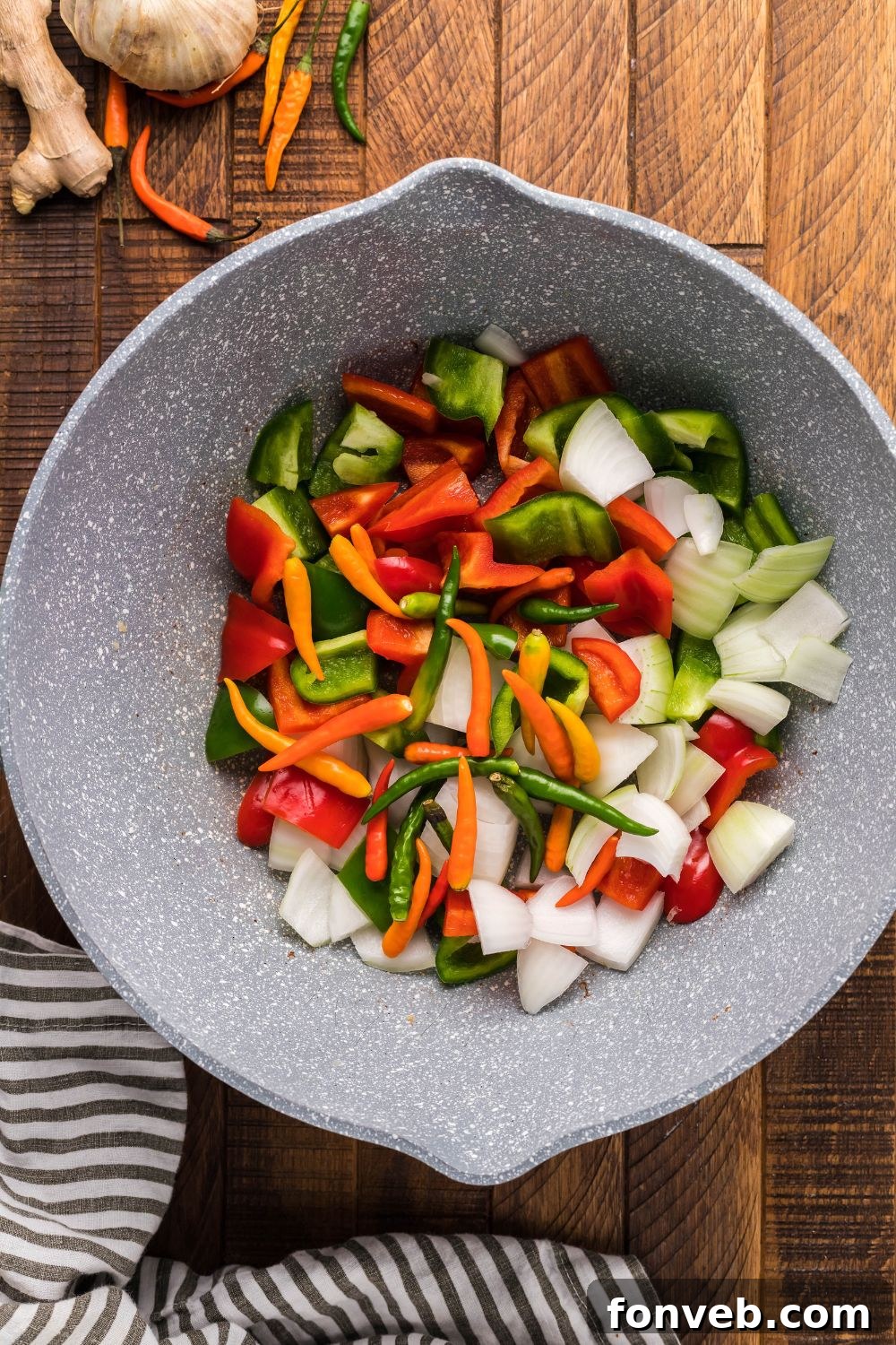 Freshly chopped vegetables, including bell peppers and onions, neatly arranged in a bowl on a table.