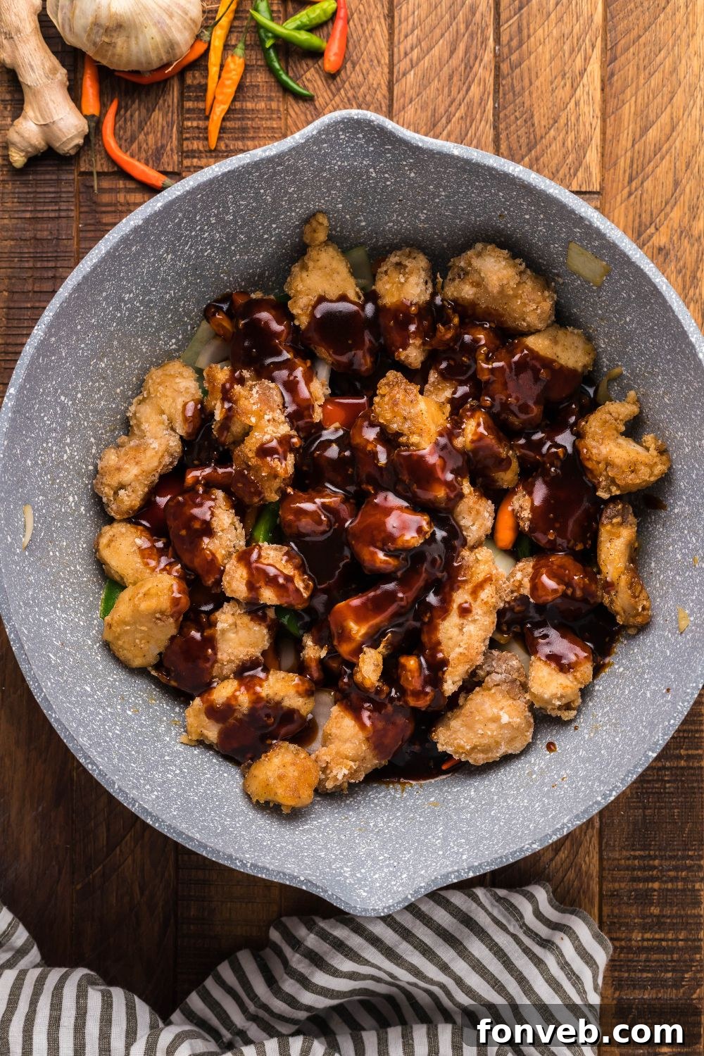A stream of glossy General Tso sauce being drizzled over cooked chicken in a pan.