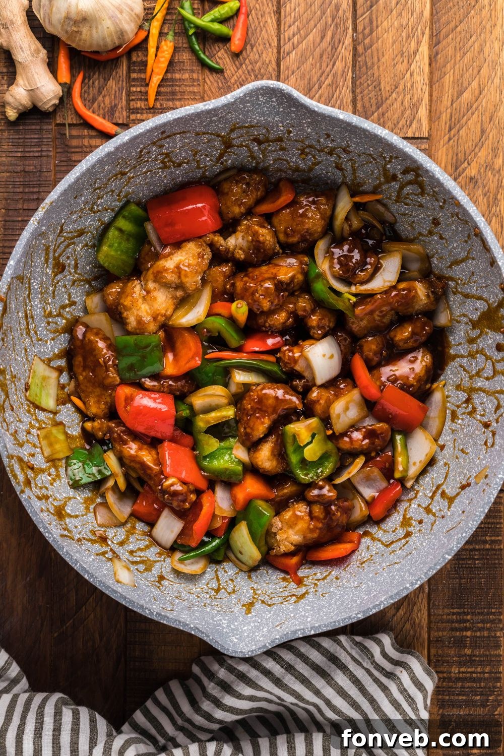 General Tso Chicken and vegetables being tossed vigorously in a bowl, ensuring every piece is coated in the rich sauce.