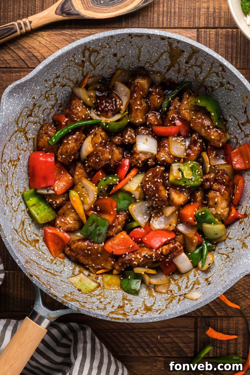 General Tso Chicken vigorously tossed in sauce with mixed vegetables in a skillet, ensuring every piece is coated.