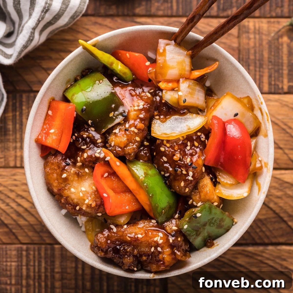 A bowl filled with freshly made General Tso Chicken, showing the crispy texture and glistening sauce, with serving tongs on the side.