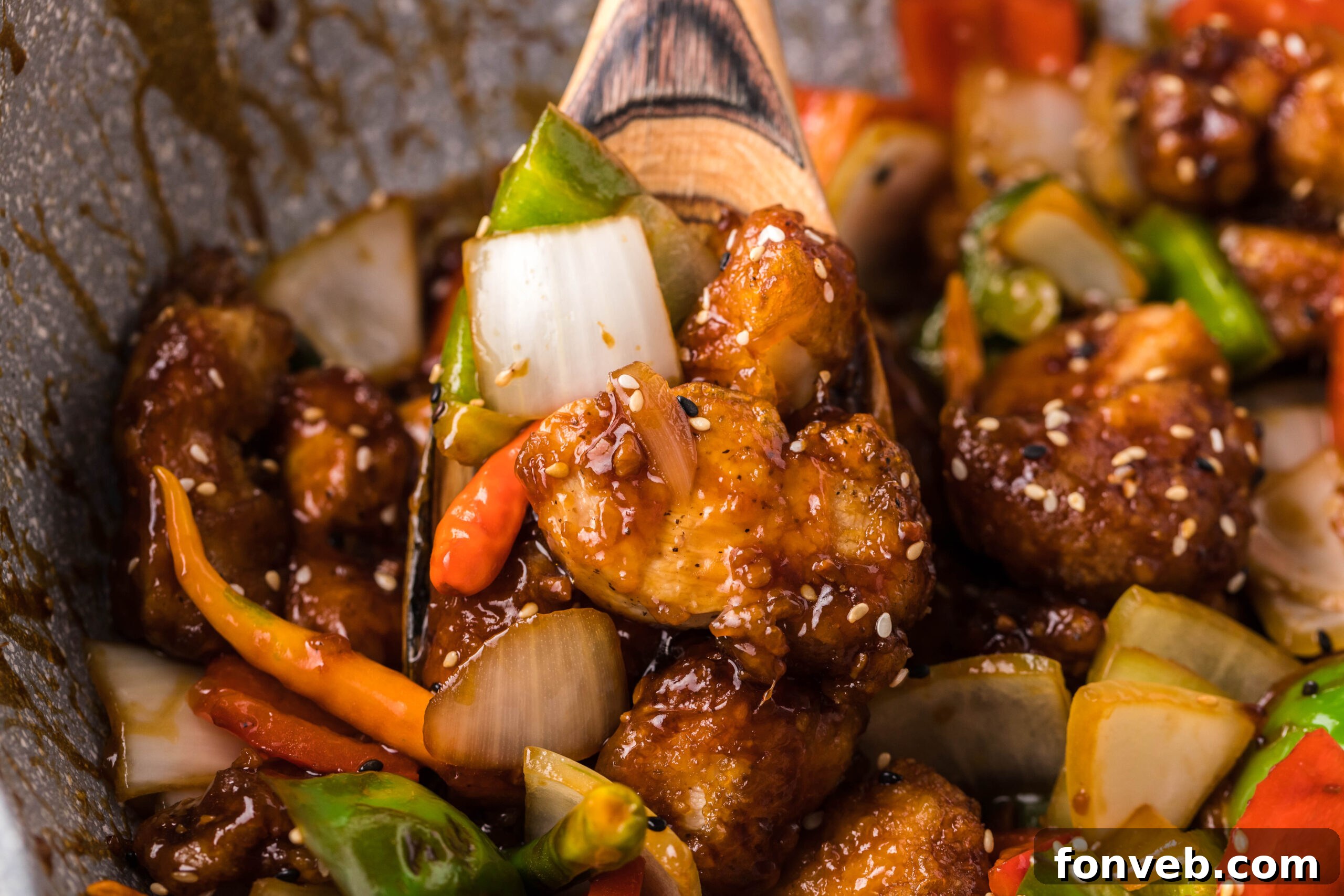 A spoon lifting a piece of General Tso Chicken, highlighting the sticky sauce and tender chicken.